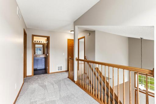 The upstairs hallway leads to the bedrooms and a full bath, with an oak railing that looks out over the vaulted entry.