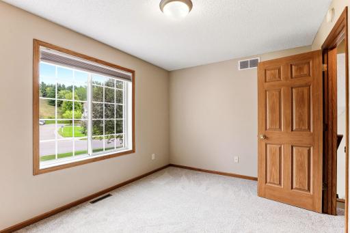 A wide picture window frames tree-lined views in this bedroom, with fresh carpet and plenty of wall space for a bed and dresser.