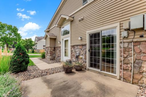 Morning coffee belongs on this patio. Sliding doors open from the dining area to a sunny concrete pad, planters, and a grassy view beyond the walkway.