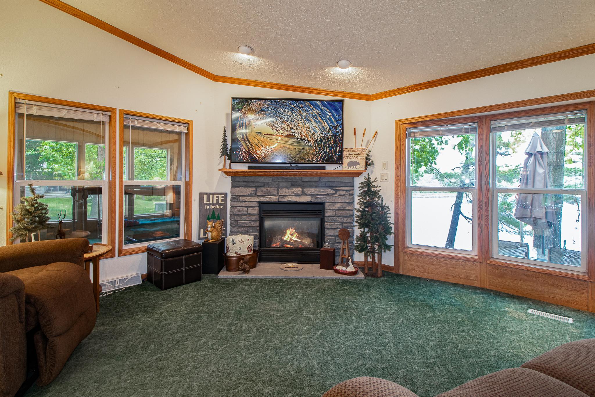 Living area with gas fireplace and large lakeside windows to the right. To the left are windows to three season porch.