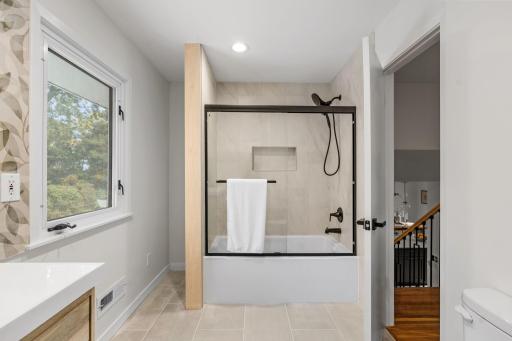 Relax in the updated shower and tub combination featuring elegant tilework, a built-in niche, and striking matte-black fixtures.