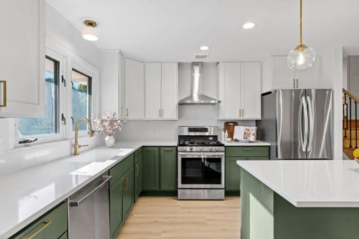This beautifully updated kitchen pairs rich green cabinetry with crisp white finishes, gold accents, and stainless-steel appliances for a fresh, modern look
