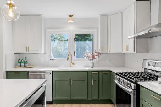 White and green cabinetry, quartz-style countertops, gold accents, and stainless-steel appliances give this kitchen a polished, contemporary feel.