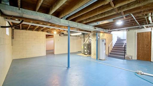 The doorway on the left features a versatile, large storage room that could easily serve as a future bedroom or dedicated home office. Stairway to the right leads to the main level kitchen and a convenient second entry.