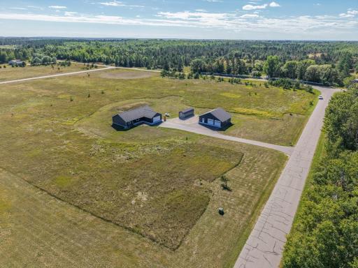 Aerial view showing the home's setting, acreage, outbuildings and paved driveway.