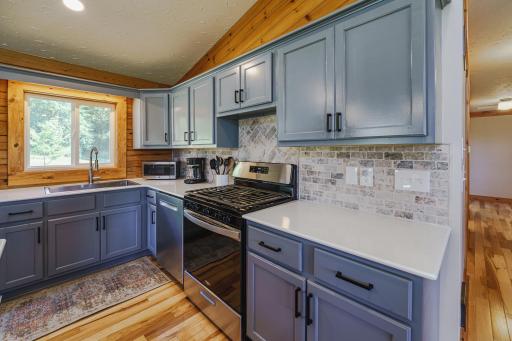 The new stainless steel appliances include a BOSCH dishwasher, and a NEW Whirlpool refrigerator and gas range in 2025. The stainless steel sink has a gooseneck faucet and looks out to the drive.