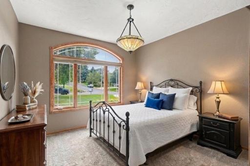 Second main level bedroom with arched window, carpet, and views of the quiet private drive. Virtually staged to show potential layout.