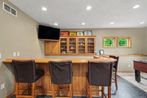 Lower level wet bar with cabinetry, counter seating, and storage, positioned between the family area and theater room.