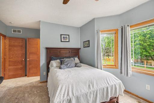 Lower level bedroom with walk-in closet, carpet, ceiling fan, and two windows overlooking the yard.
