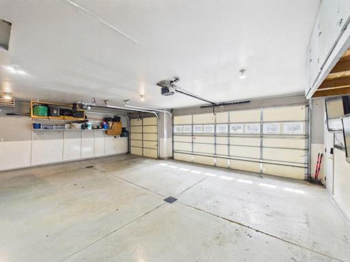 Interior view of the heated 3-car garage with multiple parking bays, storage shelving, and floor drain.