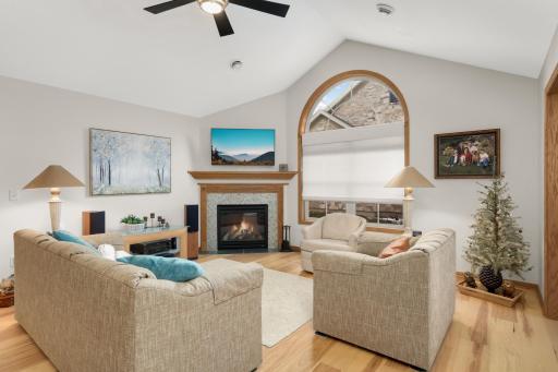 Inviting living room with a vaulted ceiling, beautiful arched window, and gas fireplace