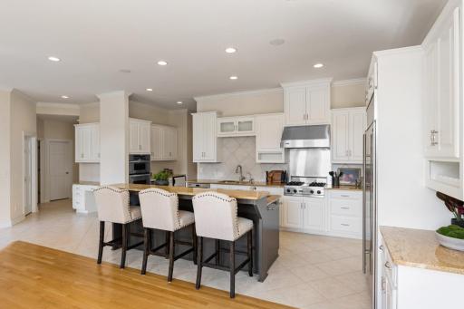 Another view of the spacious kitchen showcasing the freshly painted white cabinetry, large contrasting center island with seating, and open layout ideal for entertaining.