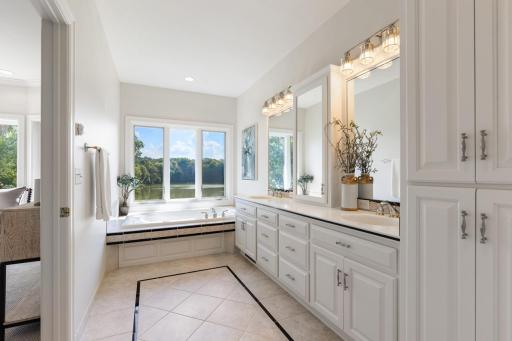 Bright and spacious primary bath featuring dual vanities, abundant cabinetry, and a relaxing soaking tub perfectly positioned to enjoy serene Turtle Pond views.