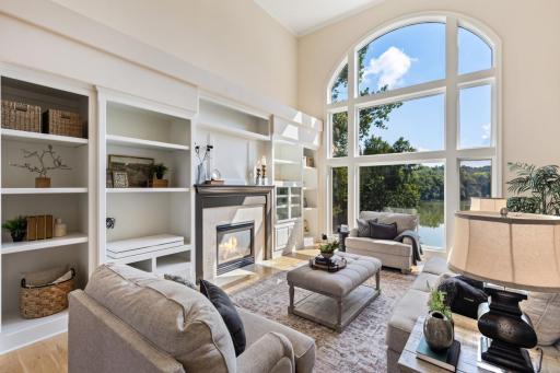 Dramatic two-story great room featuring soaring windows, custom built-ins, a cozy fireplace.