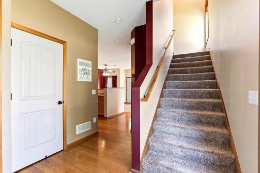 Inviting main-level hallway with hardwood floors, warm wood trim, and a carpeted staircase leading to the upper level.