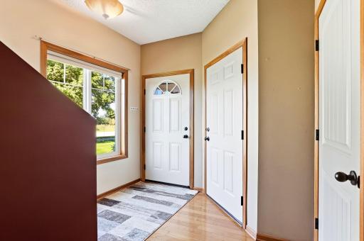 Bright, welcoming entryway featuring hardwood floors, warm wood trim, a large window for natural light, and a convenient coat closet.