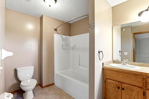Full primary en-suite bathroom featuring a tub/shower combination, spacious vanity, large mirror, and warm wood cabinetry.