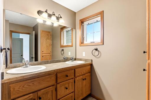 Private primary bathroom featuring a spacious dual-sink vanity, ample cabinetry, large mirror, linen closet, and natural light.