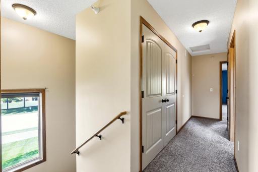 Bright upper-level hallway with plush carpeting, warm wood trim, laundry closet, and natural light from the stairway window.