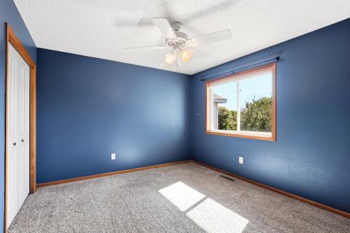 Bright upper-level bedroom featuring plush carpeting, a ceiling fan, spacious closet, and a large window providing plenty of natural light.