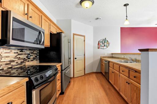 Functional kitchen with abundant cabinetry and counter space, stainless steel appliances, tile backsplash, hardwood floors, breakfast bar, and convenient pantry.