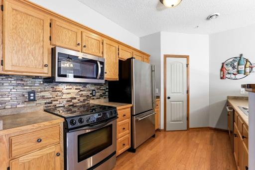Well-appointed kitchen featuring warm wood cabinetry, stainless steel appliances, tile backsplash, ample counter space, and hardwood flooring.