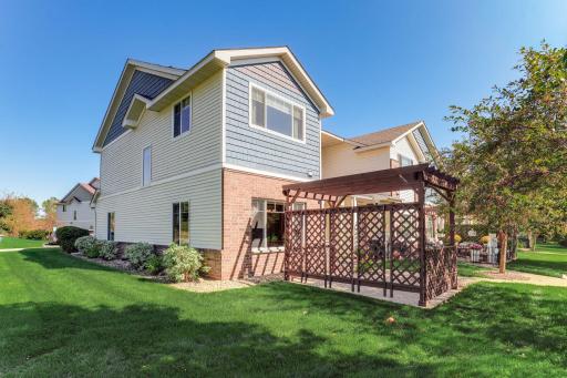 Desirable end-unit exterior with expansive green space, mature landscaping, and a private patio with pergola and added lattice panels for enhanced privacy.