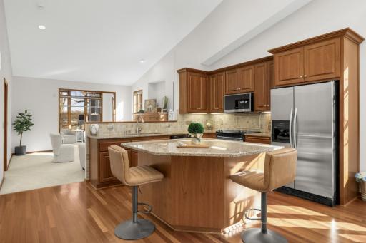 Open-concept kitchen with granite center island, stainless steel appliances, hardwood floors, and seamless flow to the living area