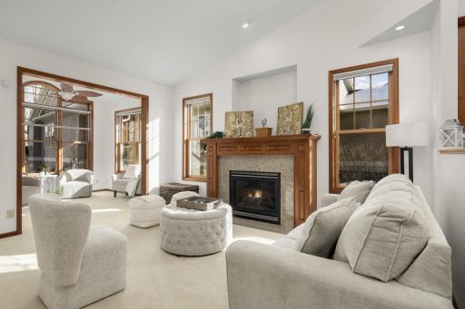 Sun-filled living room with cozy gas fireplace, expansive windows, and vaulted ceilings overlooking the natural setting.