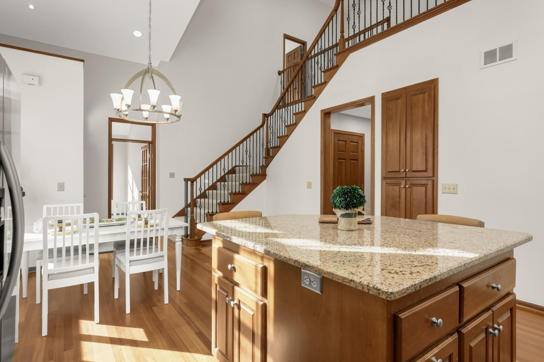 Open-concept kitchen and dining area with granite island, soaring ceilings, hardwood floors, and dramatic staircase detail.