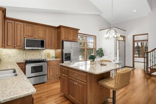 Bright, vaulted kitchen with granite countertops, center island seating, stainless steel appliances, and warm hardwood floors in Maple Grove.