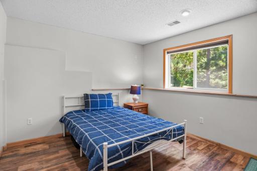 Comfortable lower-level master bedroom with updated flooring, a large window, and peaceful views of the surrounding trees.