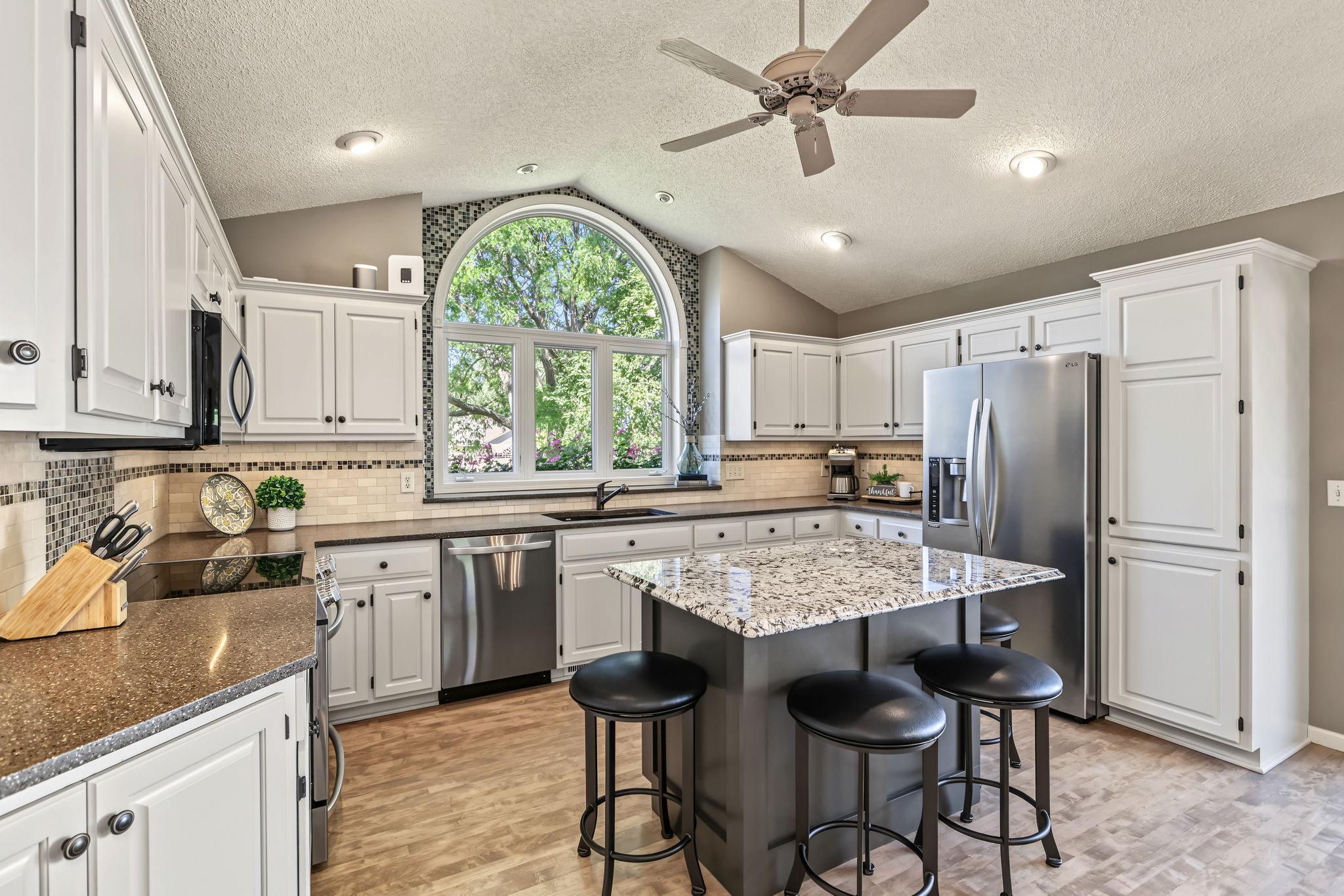 Crisp white cabinetry provides a timeless fresh feel, beautifully complemented by stainless steel appliances and warm maple hardwood flooring.