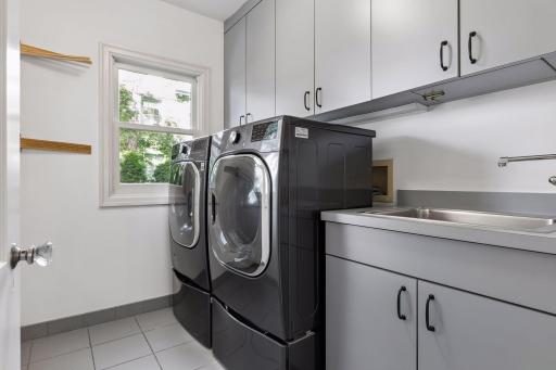 Main level laundry is located off of a back hall near the kitchen and secondary "back" staircase. A laundry chute delivers items to the cabinetry above the laundry sink.