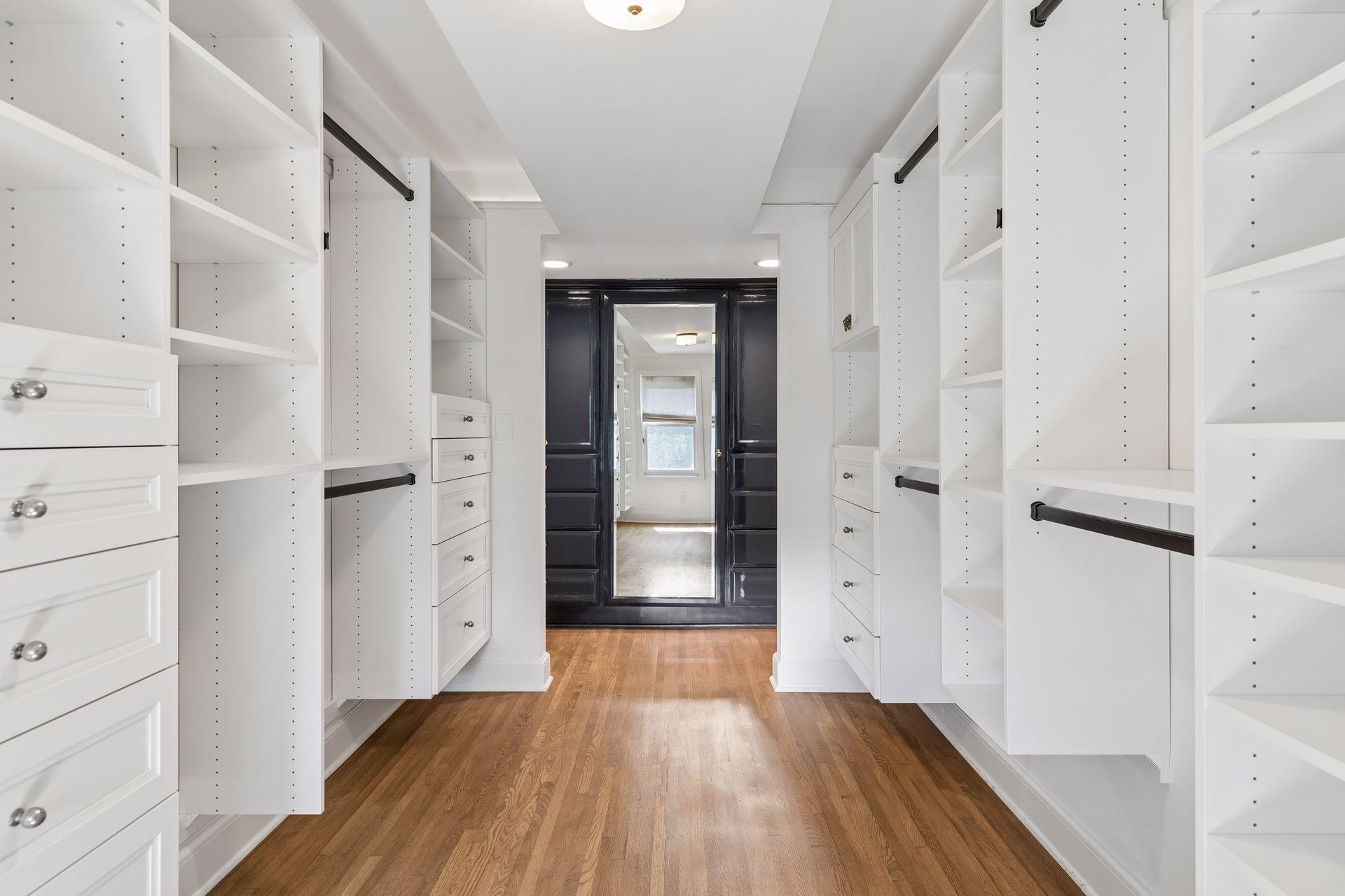 Large walk-in closet with additional enameled cabinets and dressing mirror.
