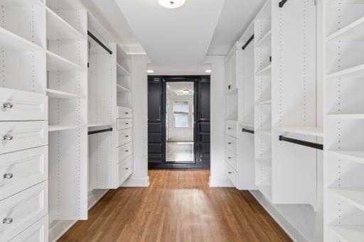 Large walk-in closet with additional enameled cabinets and dressing mirror.
