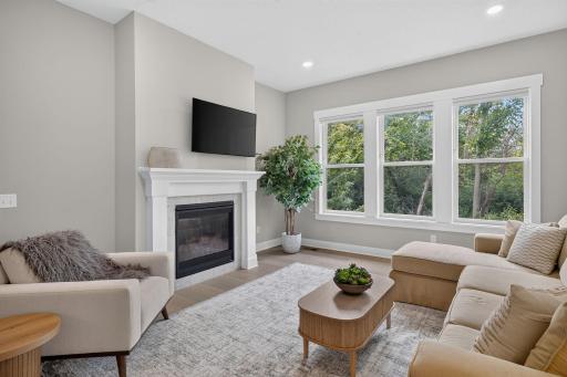 The inviting living room with gas fireplace and expansive windows overlooks the wooded backyard