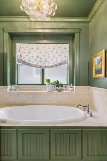 A quiet soaking tub sits beneath a window, surrounded by rich cabinetry and classic details.