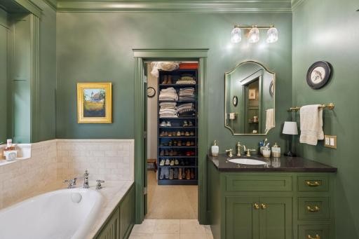 The primary bath pairs warm green cabinetry with a soaking tub and generous storage.