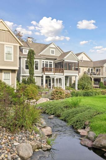 The rear exterior features layered outdoor living spaces overlooking the gardens and creek.
