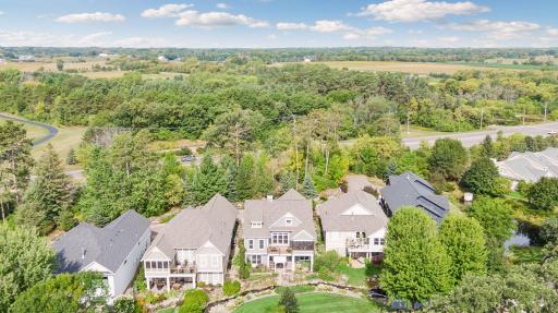 A wider aerial view captures the home, creek, mature landscaping, and neighboring architecture.