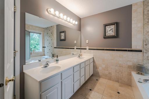 The adjoined private bathroom includes a white vanity with dual sinks, a soaking tub, HEATED TILE FLOORING, and travertine walls.