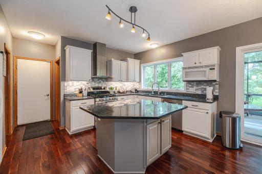 The kitchen was remodeled to include staggered white cabinetry with granite surfaces, a custom tile backsplash, a gas range with a vent hood, and a new sink.