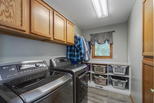 The laundry room has plank vinyl flooring, a bright window and stainless steel washer/dryer.