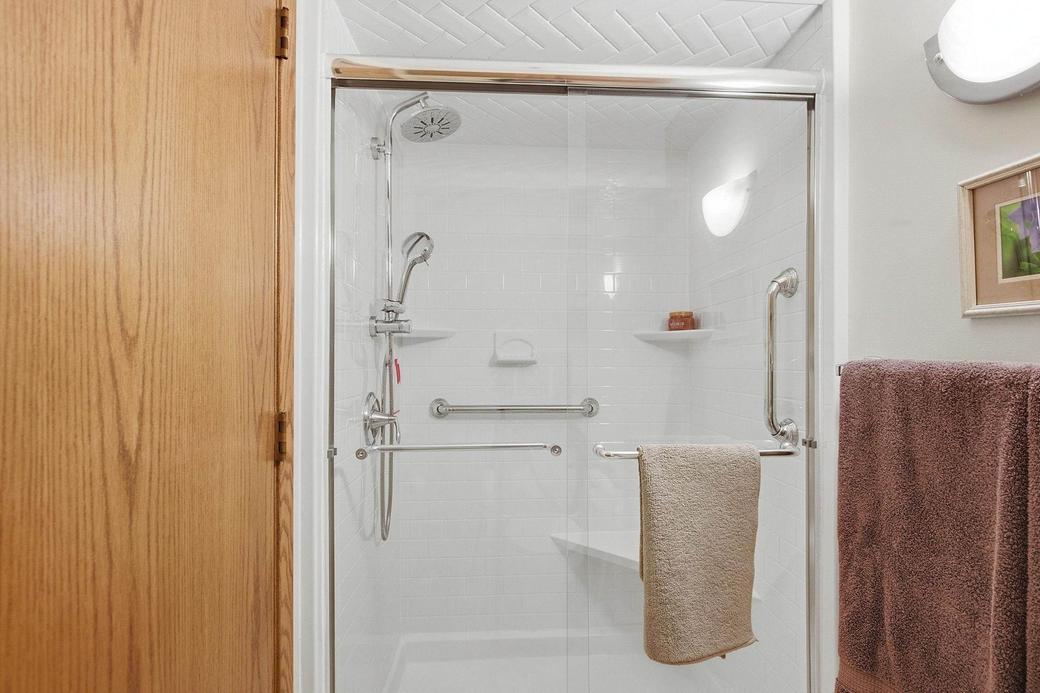 Primary Suite Walk-In Shower - Updated shower features a glass enclosure, multiple shower heads, built-in corner seating, and grab bars for added convenience.