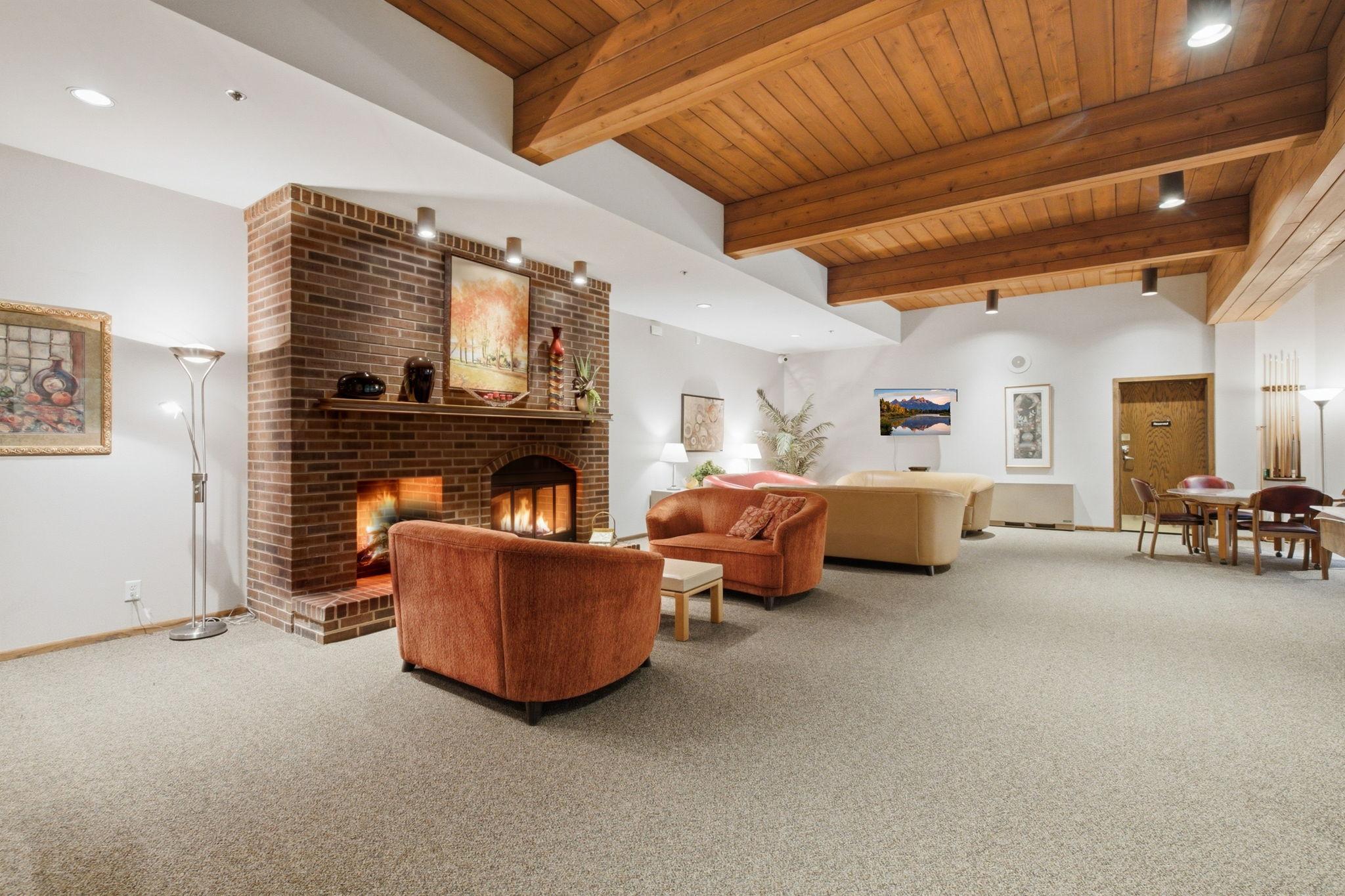 Community Room - Spacious resident gathering room features a dramatic wood-beamed ceiling, brick fireplace, multiple seating areas, and tables for socializing and community activities.