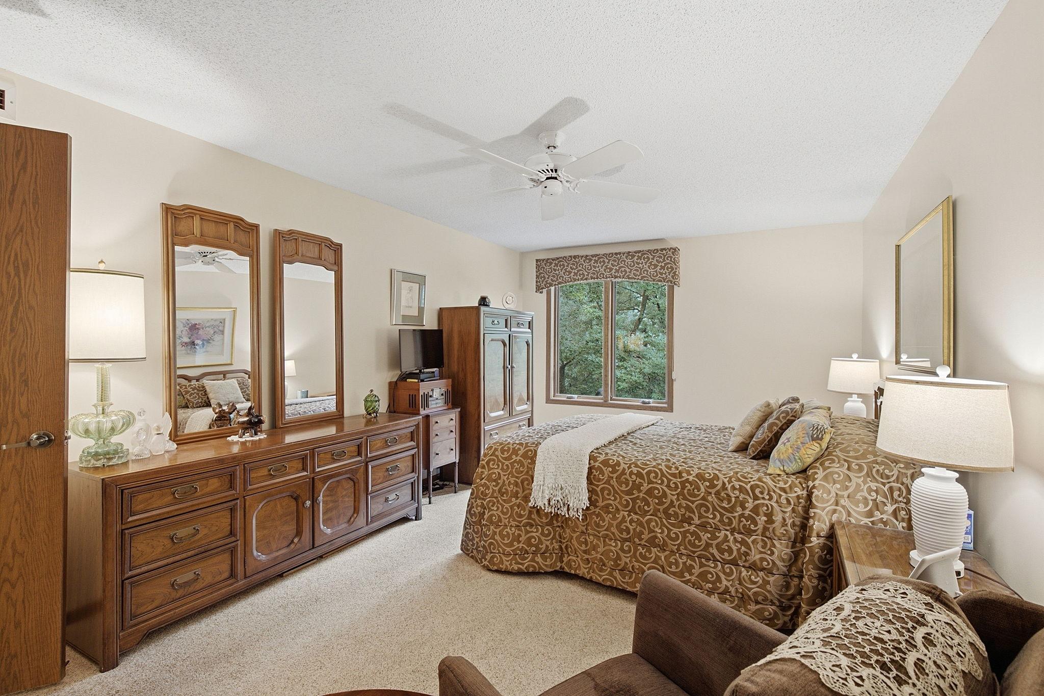 Primary Bedroom - Spacious primary bedroom offers plenty of room for a large bed and additional furniture, plus a ceiling fan and window overlooking the mature trees.