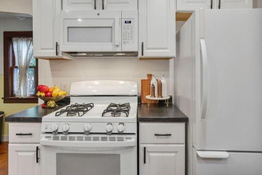 Gas range and built-in microwave surrounded by crisp white cabinetry and generous counter space.