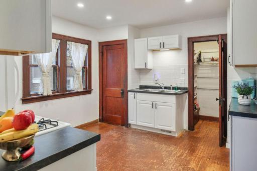 Bright kitchen with white cabinetry, dark countertops, recessed lighting, and original wood window trim.