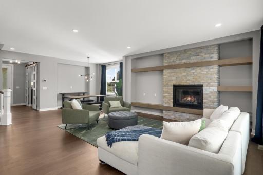 Spacious living room highlighted by a statement fireplace, brick surround, custom floating shelves, and hardwood floors.